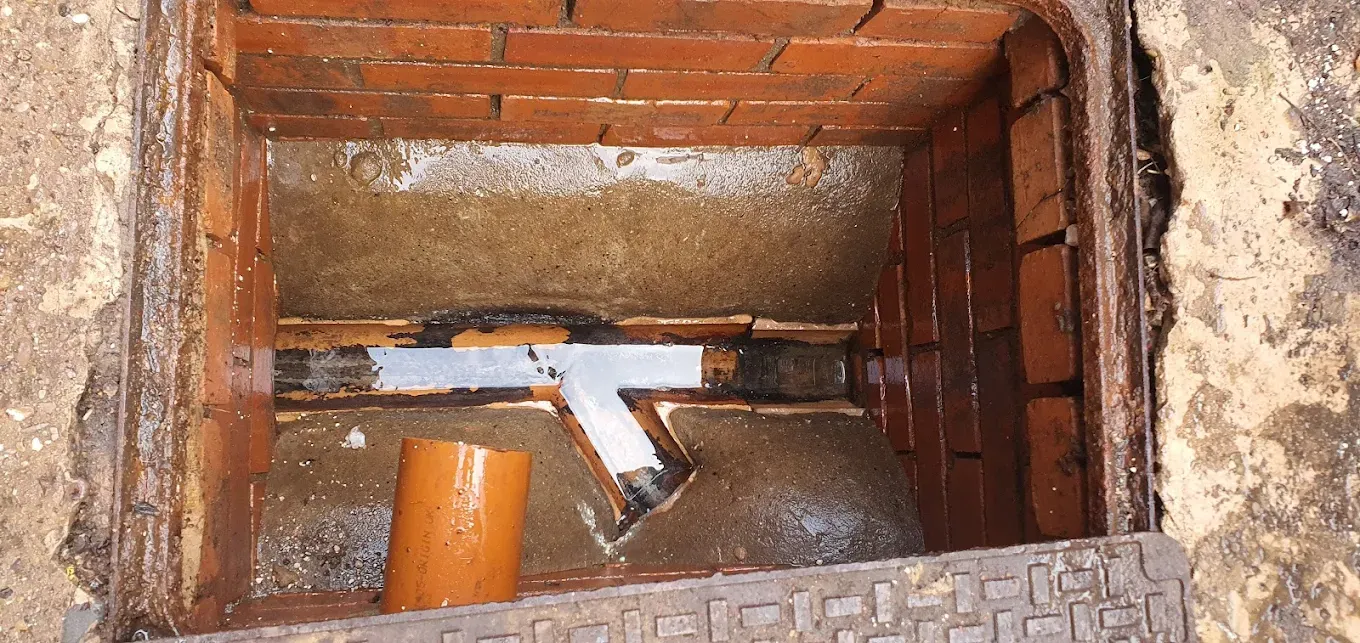 Blocked drain manhole with standing water and orange pipe segment